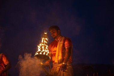Varanasi, Uttar Pradesh, Hindistan - Kasım 2022: Ganga aarti, genç bir rahibin portresi, Assi Ghat 'ta akşam üzeri ateş ve ayinlerle geleneksel elbise giymiş nehir çetelerini icra ediyor..