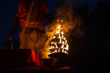 Varanasi, Uttar Pradesh, Hindistan - Kasım 2022: Ganga aarti, genç bir rahibin portresi, Assi Ghat 'ta akşam üzeri ateş ve ayinlerle geleneksel elbise giymiş nehir çetelerini icra ediyor..