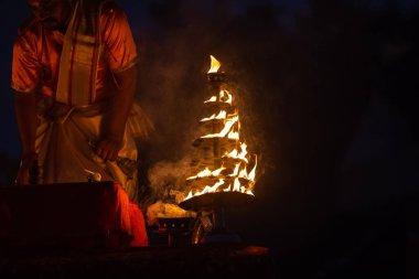 Varanasi, Uttar Pradesh, Hindistan - Kasım 2022: Ganga aarti, genç bir rahibin portresi, Assi Ghat 'ta akşam üzeri ateş ve ayinlerle geleneksel elbise giymiş nehir çetelerini icra ediyor..