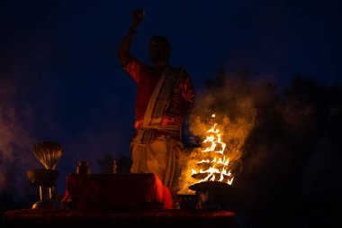 Varanasi, Uttar Pradesh, Hindistan - Kasım 2022: Ganga aarti, genç bir rahibin portresi, Assi Ghat 'ta akşam üzeri ateş ve ayinlerle geleneksel elbise giymiş nehir çetelerini icra ediyor..
