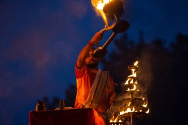 Varanasi, Uttar Pradesh, Hindistan - Kasım 2022: Ganga aarti, genç bir rahibin portresi, Assi Ghat 'ta akşam üzeri ateş ve ayinlerle geleneksel elbise giymiş nehir çetelerini icra ediyor..