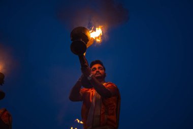 Varanasi, Uttar Pradesh, Hindistan - Kasım 2022: Ganga aarti, genç bir rahibin portresi, Assi Ghat 'ta akşam üzeri ateş ve ayinlerle geleneksel elbise giymiş nehir çetelerini icra ediyor..