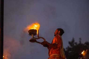 Varanasi, Uttar Pradesh, Hindistan - Kasım 2022: Ganga aarti, genç bir rahibin portresi, Assi Ghat 'ta akşam üzeri ateş ve ayinlerle geleneksel elbise giymiş nehir çetelerini icra ediyor..