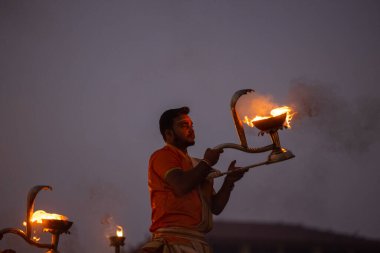 Varanasi, Uttar Pradesh, Hindistan - Kasım 2022: Ganga aarti, genç bir rahibin portresi, Assi Ghat 'ta akşam üzeri ateş ve ayinlerle geleneksel elbise giymiş nehir çetelerini icra ediyor..
