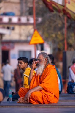 Varanasi, Uttar Pradesh, Hindistan - 20 Kasım 2022: Varanasi şehrinde geleneksel elbise içinde nehir çetelerinin yanında oturan kimliği belirsiz kutsal Hint sadhu erkeği portresi.