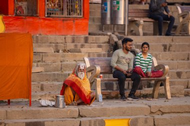 Varanasi, Uttar Pradesh, Hindistan - 20 Kasım 2022: Varanasi şehrinde geleneksel elbise içinde nehir çetelerinin yanında oturan kimliği belirsiz kutsal Hint sadhu erkeği portresi.