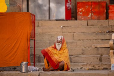 Varanasi, Uttar Pradesh, Hindistan - 20 Kasım 2022: Varanasi şehrinde geleneksel elbise içinde nehir çetelerinin yanında oturan kimliği belirsiz kutsal Hint sadhu erkeği portresi.