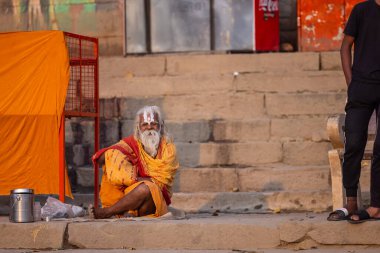 Varanasi, Uttar Pradesh, Hindistan - 20 Kasım 2022: Varanasi şehrinde geleneksel elbise içinde nehir çetelerinin yanında oturan kimliği belirsiz kutsal Hint sadhu erkeği portresi.