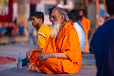 Varanasi, Uttar Pradesh, Hindistan - 20 Kasım 2022: Varanasi şehrinde geleneksel elbise içinde nehir çetelerinin yanında oturan kimliği belirsiz kutsal Hint sadhu erkeği portresi.