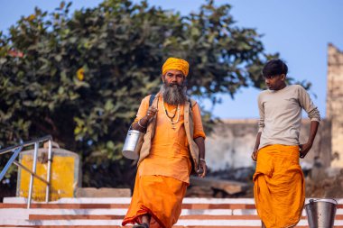 Varanasi, Uttar Pradesh, Hindistan - 20 Kasım 2022: Varanasi şehrinde geleneksel elbise içinde nehir çeteleri yakınında yürüyen kimliği belirsiz kutsal Hint sadhu erkeklerinin portresi.