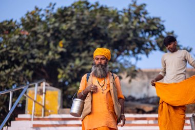 Varanasi, Uttar Pradesh, Hindistan - 20 Kasım 2022: Varanasi şehrinde geleneksel elbise içinde nehir çeteleri yakınında yürüyen kimliği belirsiz kutsal Hint sadhu erkeklerinin portresi.