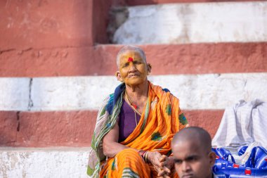 Varanasi, Uttar Pradesh, Hindistan - 20 Kasım 2022: Geleneksel saride kedar ghat merdivenlerinde kafası tıraşlı yaşlı bir Hintli kadının portresi. Kel kafa, kashi 'de yapılan bir ayindir..