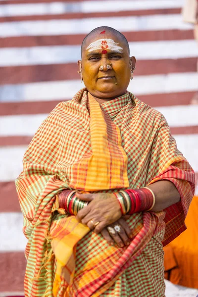 stock image Varanasi, Uttar Pradesh, India - November 20 2022: Portrait on an old south indian woman with shaved head sitting on stairs at kedar ghat in traditional saree. Bald head is ritual performed in kashi.