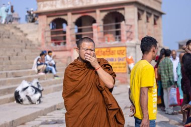 Varanasi, Uttar Pradesh, Hindistan - 20 Kasım 2022: Varanasi şehrinde geleneksel elbise içinde nehir çeteleri yakınında yürüyen kimliği belirsiz bir Budist keşişin portresi.