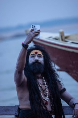 Varanasi, Uttar Pradesh, Hindistan - 20 Kasım 2022: Naga sadhu olarak tanımlanamayan Hintli erkek aktörün portresi ve Varanasi 'deki nehir çetelerinin ahşap teknesinde oturan yüzü ve vücudu soruldu.