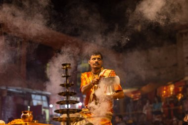 Varanasi, Uttar Pradesh, Hindistan - 20 Kasım 2022: Ganga aarti, Dashashwamedh ghat 'ında geleneksel Hint ayinleriyle akşam üzeri genç rahibin kutsal nehir çetelerini sergilediği portre.
