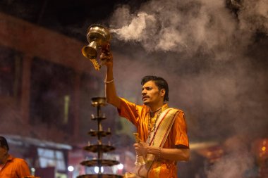 Varanasi, Uttar Pradesh, Hindistan - 20 Kasım 2022: Ganga aarti, Dashashwamedh ghat 'ında geleneksel Hint ayinleriyle akşam üzeri genç rahibin kutsal nehir çetelerini sergilediği portre.