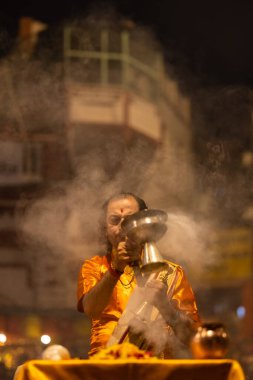 Varanasi, Uttar Pradesh, Hindistan - 20 Kasım 2022: Ganga aarti, Dashashwamedh ghat 'ında geleneksel Hint ayinleriyle akşam üzeri genç rahibin kutsal nehir çetelerini sergilediği portre.