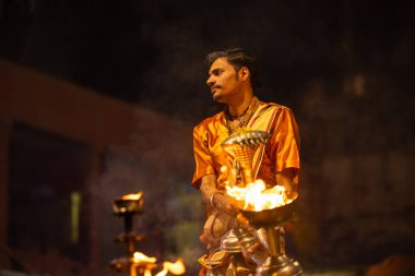 Varanasi, Uttar Pradesh, Hindistan - 20 Kasım 2022: Ganga aarti, Dashashwamedh ghat 'ında geleneksel Hint ayinleriyle akşam üzeri genç rahibin kutsal nehir çetelerini sergilediği portre.
