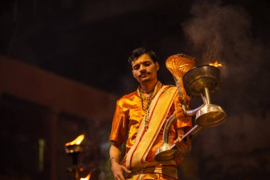 Varanasi, Uttar Pradesh, Hindistan - 20 Kasım 2022: Ganga aarti, Dashashwamedh ghat 'ında geleneksel Hint ayinleriyle akşam üzeri genç rahibin kutsal nehir çetelerini sergilediği portre.
