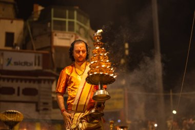 Varanasi, Uttar Pradesh, Hindistan - 20 Kasım 2022: Ganga aarti, Dashashwamedh ghat 'ında geleneksel Hint ayinleriyle akşam üzeri genç rahibin kutsal nehir çetelerini sergilediği portre.