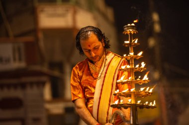 Varanasi, Uttar Pradesh, Hindistan - 20 Kasım 2022: Ganga aarti, Dashashwamedh ghat 'ında geleneksel Hint ayinleriyle akşam üzeri genç rahibin kutsal nehir çetelerini sergilediği portre.