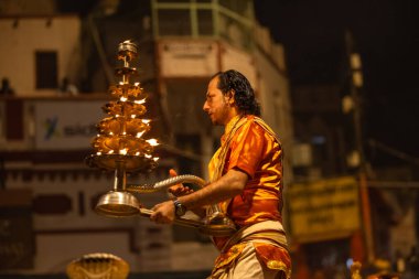 Varanasi, Uttar Pradesh, Hindistan - 20 Kasım 2022: Ganga aarti, Dashashwamedh ghat 'ında geleneksel Hint ayinleriyle akşam üzeri genç rahibin kutsal nehir çetelerini sergilediği portre.
