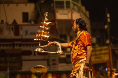 Varanasi, Uttar Pradesh, Hindistan - 20 Kasım 2022: Ganga aarti, Dashashwamedh ghat 'ında geleneksel Hint ayinleriyle akşam üzeri genç rahibin kutsal nehir çetelerini sergilediği portre.