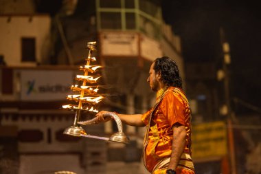 Varanasi, Uttar Pradesh, Hindistan - 20 Kasım 2022: Ganga aarti, Dashashwamedh ghat 'ında geleneksel Hint ayinleriyle akşam üzeri genç rahibin kutsal nehir çetelerini sergilediği portre.