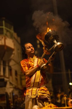 Varanasi, Uttar Pradesh, Hindistan - 20 Kasım 2022: Ganga aarti, Dashashwamedh ghat 'ında geleneksel Hint ayinleriyle akşam üzeri genç rahibin kutsal nehir çetelerini sergilediği portre.