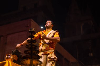 Varanasi, Uttar Pradesh, Hindistan - 20 Kasım 2022: Ganga aarti, Dashashwamedh ghat 'ında geleneksel Hint ayinleriyle akşam üzeri genç rahibin kutsal nehir çetelerini sergilediği portre.