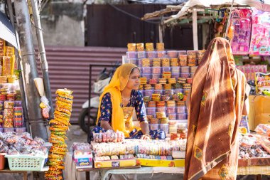 Pushkar, Rajasthan, Hindistan - 05 Kasım 2022: Pushkar 'da dükkanın önünde oturan bir kadın sokak satıcısı. Pushkar sokak pazarı yerli halk ve turistler arasında geleneksel giysi ve ürünleriyle popüler.