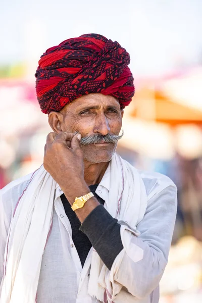 Stock image Pushkar, Rajasthan, India - November 05 2022: Pushkar fair, Portrait of an rajasthani old male with in white traditional dress and colorful turban touching his moustache at pushkar fair ground.