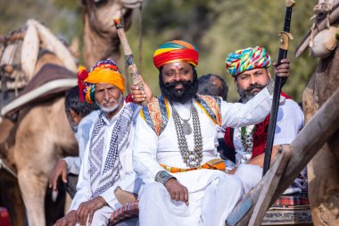 Bikaner, Rajasthan, Hindistan - 13 Ocak 2023: Deve Festivali, sakallı ve bıyıklı genç bir Rajasthani erkek portresi geleneksel rajasthani elbisesi ve deve arabasında türban sürüyor..