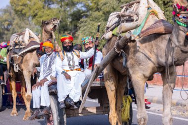 Bikaner, Rajasthan, Hindistan - 13 Ocak 2023: Deve Festivali, sakallı ve bıyıklı genç bir Rajasthani erkek portresi geleneksel rajasthani elbisesi ve deve arabasında türban sürüyor..