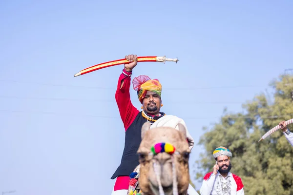 stock image Bikaner, Rajasthan, India - January 13 2023: Camel Festival, Portrait of an young rajasthani male with beard and moustache wearing white traditional rajasthani dress and turban riding on camel.
