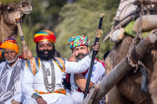 stock image Bikaner, Rajasthan, India - January 13 2023: Camel Festival, Portrait of an young rajasthani male with beard and moustache wearing white traditional rajasthani dress and turban riding on camel cart.