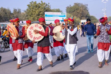 Bikaner, Rajasthan, Hindistan - 13 Ocak 2023: Deve Festivali, Rajasthani erkek bir sanatçının portresi renkli türbanla geleneksel renkli rajasthani elbiseler giyerek müzik aleti çalıyor.