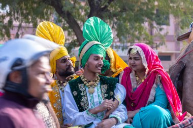 Bikaner, Rajasthan, Hindistan - 13 Ocak 2023: Punjabi Bhangra, geleneksel Punjabi renkli elbise ve takı giymiş genç sih erkek ve kadın portresi deve festivalinde bhangra dansı yapıyor.