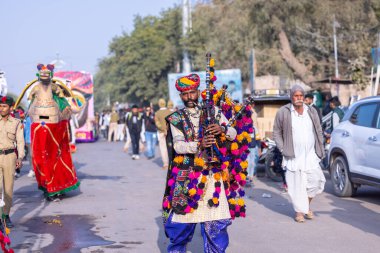 Bikaner, Rajasthan, Hindistan - 13 Ocak 2023: Deve Festivali, Rajasthani erkek bir sanatçının portresi renkli türbanla geleneksel renkli rajasthani elbiseler giyerek müzik aleti çalıyor.