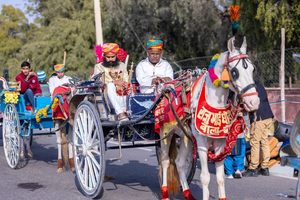 stock image Bikaner, Rajasthan, India - January 13 2023: Camel Festival, Portrait of an young rajasthani male with beard and moustache wearing white traditional rajasthani dress and turban riding on camel cart.