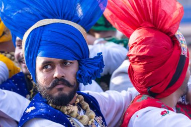 Bikaner, Rajasthan, Hindistan - 13 Ocak 2023: Punjabi Bhangra, geleneksel Punjabi renkli elbise içindeki genç sih erkek portresi ve türban deve festivalinde gülümseyerek bhangra dansı yapıyor