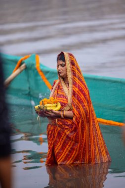 Gaziabad, Uttar Pradesh, Hindistan - 30 Ekim 2022: Chhas Puja, Hintli kadın dindar gün batımında Lord Sun 'a ibadet etmek için nehirde dururken Chhas puja ayini yapıyor..