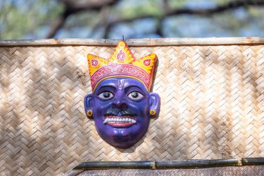 Handmade colorful tribal look face mask souvenir hanging on plain background. Selective focus on object.