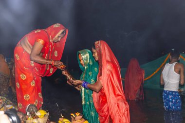 Gaziabad, Uttar Pradesh, Hindistan - 30 Ekim 2022: Chhas Puja, Hintli kadın dindar gün batımında Lord Sun 'a ibadet etmek için nehirde dururken Chhas puja ayini yapıyor..
