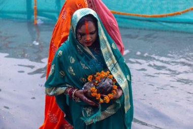 Ghaziabad, Uttar Pradesh, India - October 30 2022: Chhath Puja, Indian hindu female devotee performing rituals of chhath puja while standing in river to worship lord sun during sunset. clipart