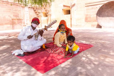 Jodhpur, Rajasthan, Hindistan - 25 Eylül 2021: Mehrangarh Kalesi, geleneksel Rajasthani elbisesiyle turistleri ağırlamak için müzik aleti çalan sanatçının portresi.