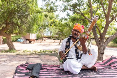 Jodhpur, Rajasthan, Hindistan - 25 Eylül 2021: Mehrangarh Kalesi, Kale binasında turistleri eğlendirmek için geleneksel Rajasthani elbisesiyle müzik aleti çalan sanatçı portresi.