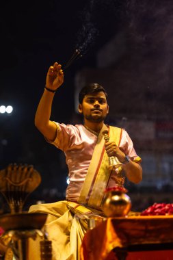 Varanasi, Uttar Pradesh, Hindistan - 3 Mart 2023: Ganga aarti, Dashashwamedh ghat geleneksel elbise ve Hindu ayinleri ile kutsal nehir ganges akşam aarti performans genç rahip portresi