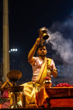 Varanasi, Uttar Pradesh, Hindistan - 3 Mart 2023: Ganga aarti, Dashashwamedh ghat geleneksel elbise ve Hindu ayinleri ile kutsal nehir ganges akşam aarti performans genç rahip portresi